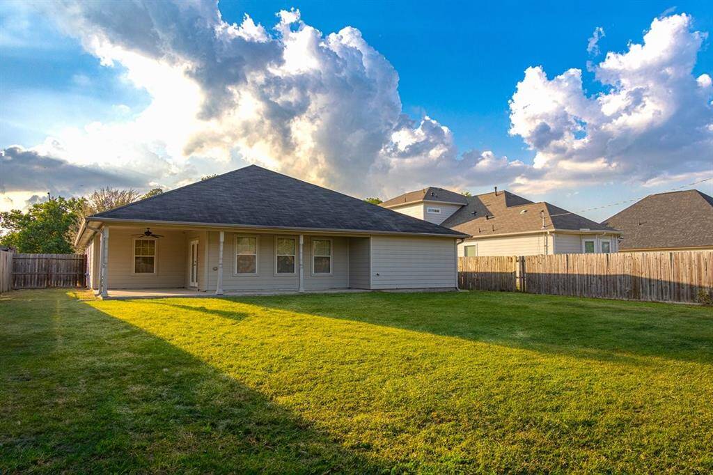 The single-story home comes with a sizable backyard, featuring a well-maintained lawn and a privacy fence. The exterior of the house has a neutral color palette, and there is a covered porch area.