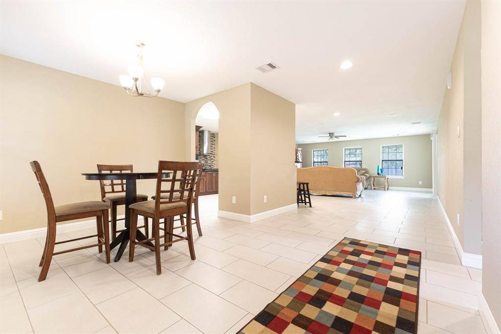 This is a spacious, open-concept interior with tiled flooring and neutral wall colors. The dining area features a chic light fixture, while an inviting living space is visible in the background, separated by an elegant arched doorway.
