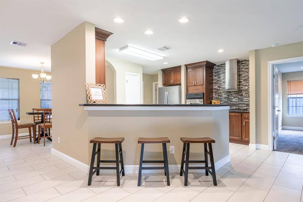 This is a modern, open-concept kitchen with a breakfast bar, featuring dark wood cabinetry, and stylish backsplash. The adjacent dining area and easy access to other rooms make it ideal for entertaining and family living.