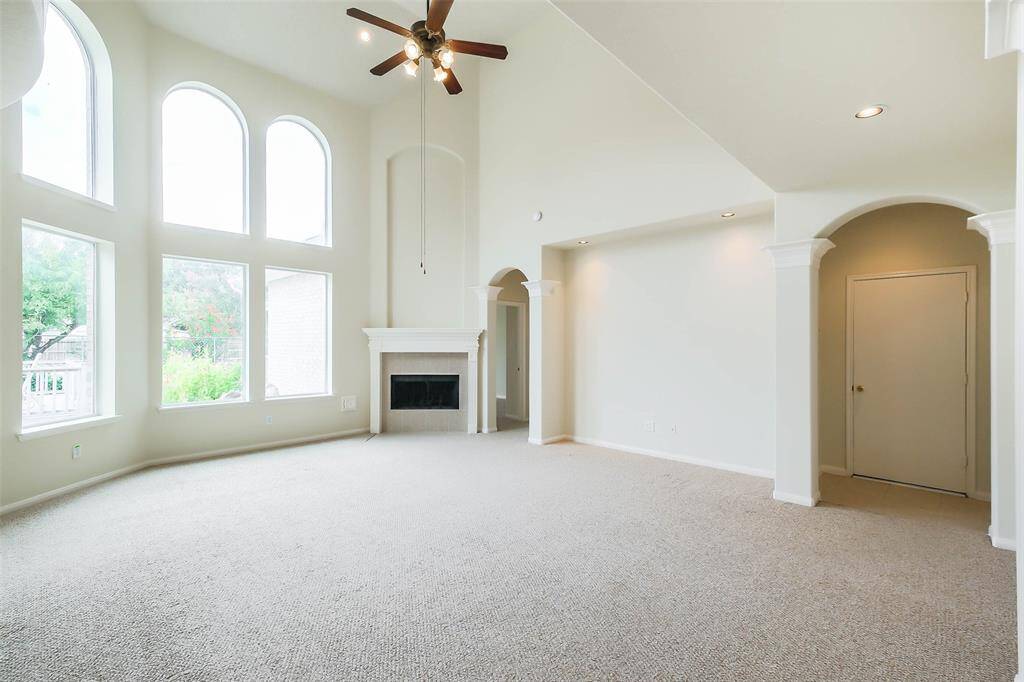 A sophisticated living room with a gas fireplace features tall glass windows, flooding the space with sunlight, showcasing a serene view of the waterfall fishpond and vibrant flowers