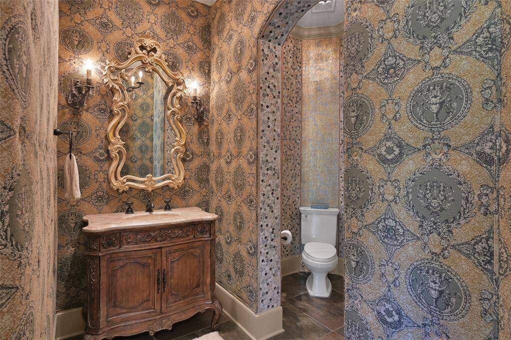 The formal half-bath showcases padded fabric walls and stunning tile accents, and an ornate mirror and vanity.
