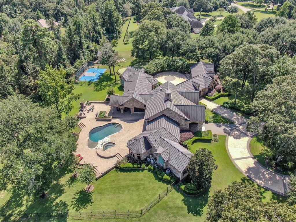 View of pool and spa, covered patio, outdoor kitchen, brick fireplace, 9-hole putting green, lighted sport court, and versatile workshop (currently a golf simulator). Front yard features a spacious circle driveway and mature trees throughout the property.