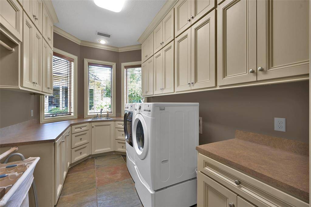Spacious laundry room overlooking courtyard equipped with ample cabinets and a convenient sink.