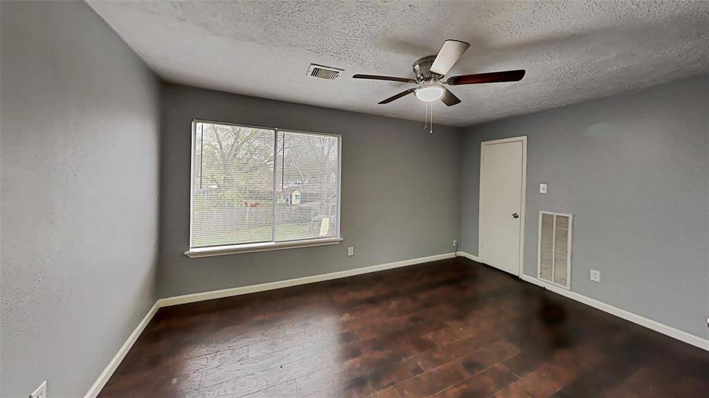 Serene Second Bedroom: Enjoy tranquil views and natural light from a large window, complete with plush hardwood floors and a modern ceiling fan.