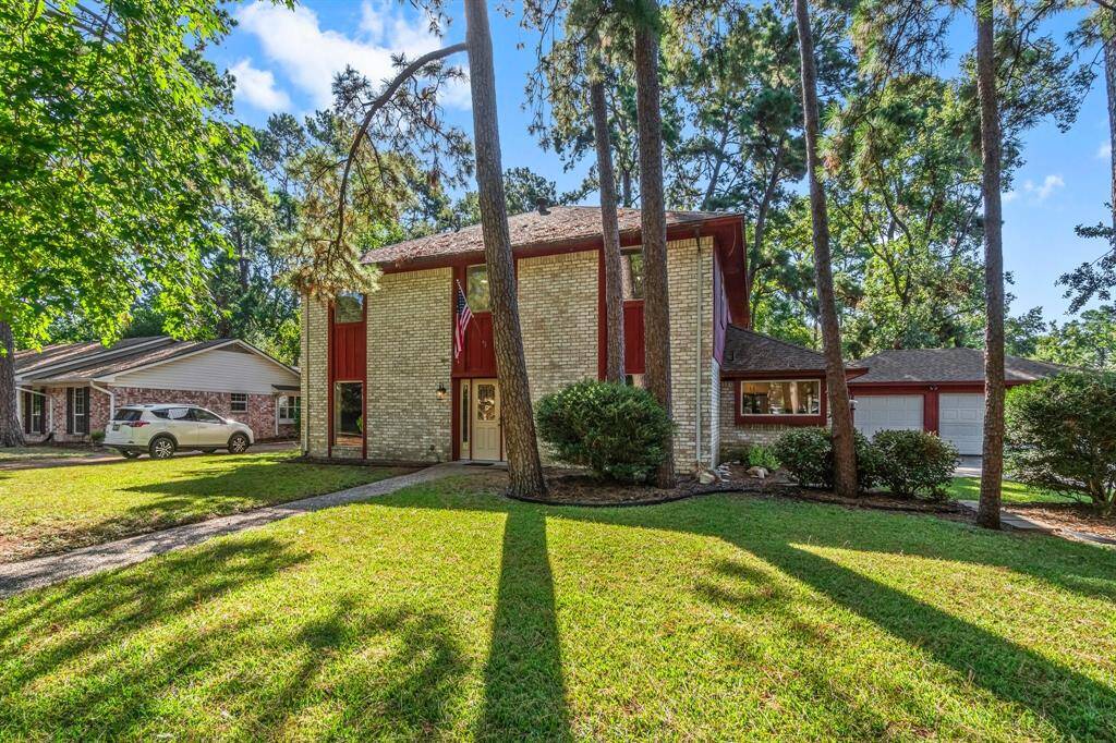 This is a two-story brick home with a red door, large windows, and an attached three-car garage, nestled among mature trees in a tranquil neighborhood.