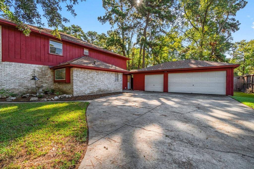 This is a two-story home featuring a red and white exterior with a spacious three-car garage and a wide driveway, set against a backdrop of mature trees.