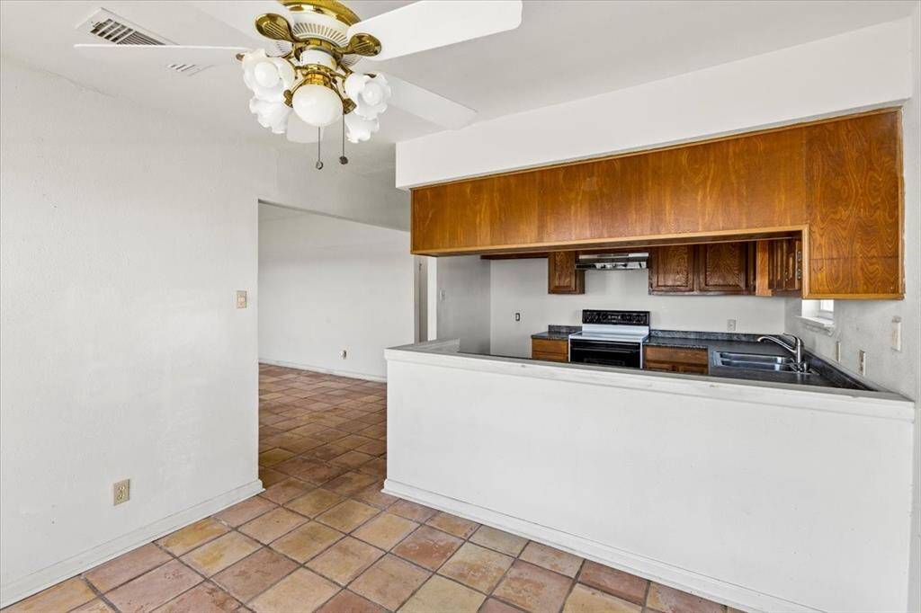 This is a spacious kitchen with wooden cabinetry and tile flooring, featuring a classic design.  There's a view into an adjacent dining area, providing an open feel.