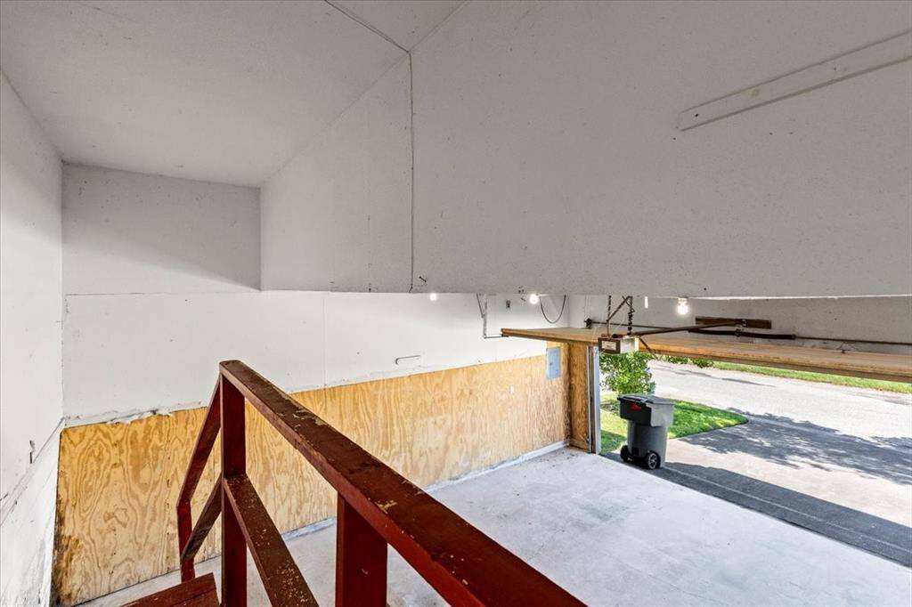 This is a two-car garage space with a simple interior, showcasing a concrete floor, white walls with some plywood paneling, and a garage door open to the driveway.