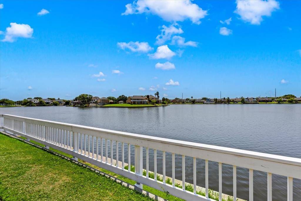 This photo showcases a serene waterfront view from a property with a white fence bordering a well-maintained lawn, offering a clear, unobstructed perspective of a tranquil lake and neighboring homes in a desirable community.