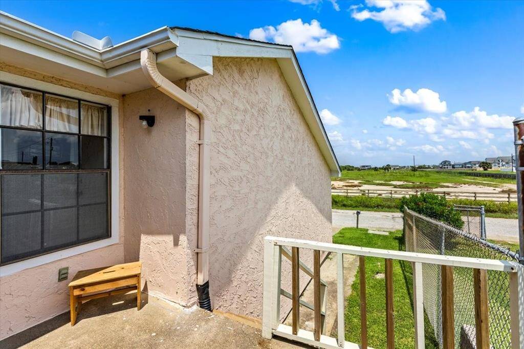 This is a view of the side entrance of the townhome featuring a small wooden step, a large window and a stucco exterior.