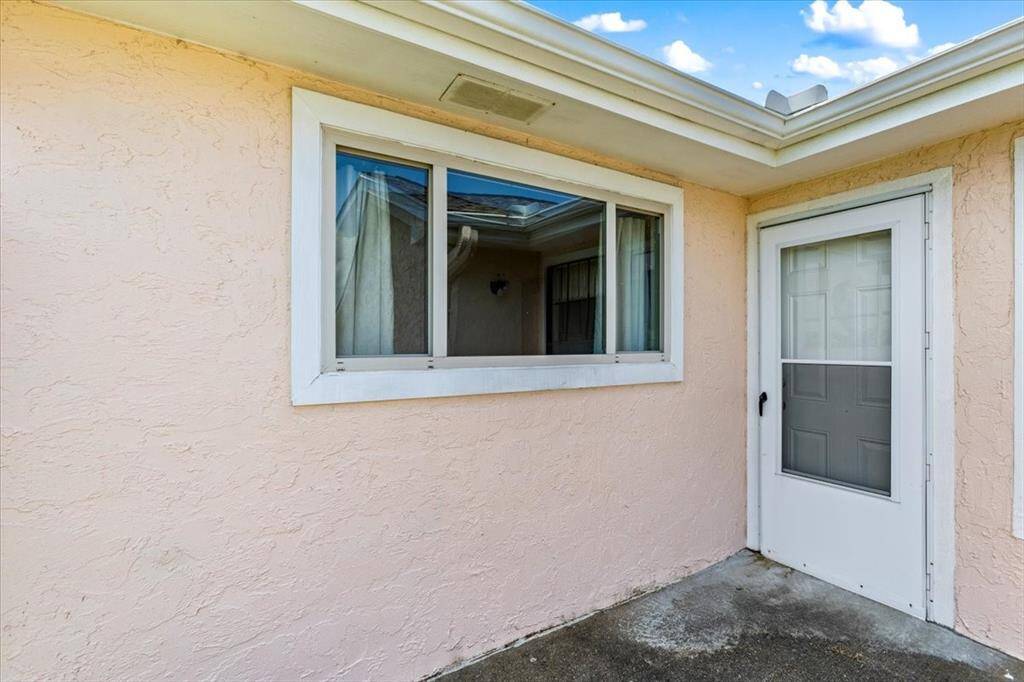 The photo shows the exterior wall and rear door entrance featuring a large window and a white door with a small window panel. The wall is finished with a textured stucco.