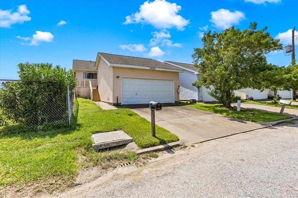The townhouse has a side entrance with a set of stairs leading up to the door and is partially fenced with a chain-link fence on one side. A mature tree in the back yard provides shade to the area.