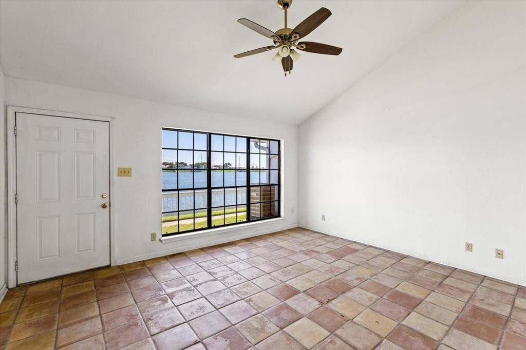This is a spacious, well-lit room with a large window offering a beautiful view of a waterfront. The room has tiled flooring and a ceiling fan.