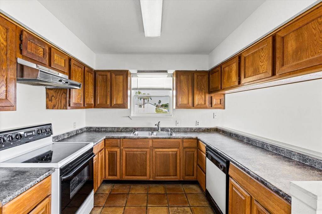 This is a functional U-shaped kitchen featuring traditional wood cabinetry, laminate countertops, and white appliances, complemented by a tile floor and a window over the sink for natural light.