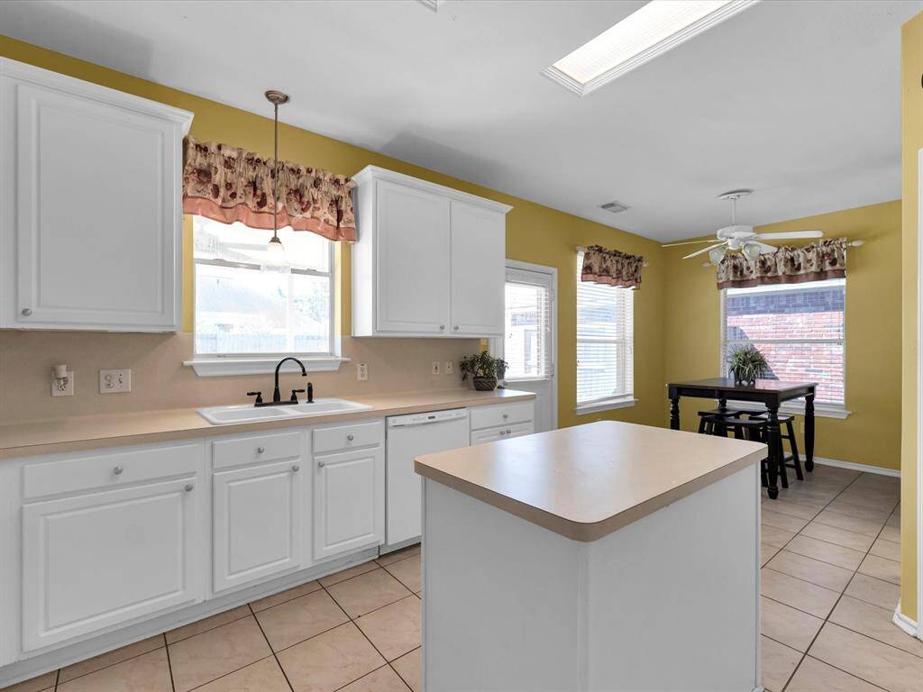 This is a bright kitchen with white cabinetry, a central island, tile flooring, and ample natural light.