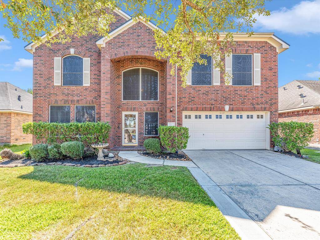 This is a two-story brick home featuring an arched entryway has large windows with solar screens for energy efficiency and a two-car garage.