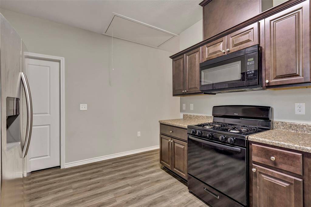 The kitchen features a gas range cooktop and oven, complemented by rich chocolate-colored cabinets offering plenty of storage. The closed door leads to the primary bedroom for easy access.