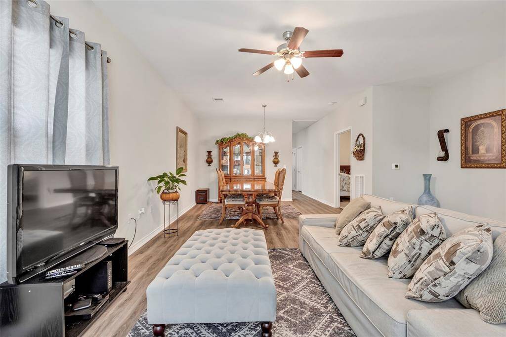 A highlight of the spacious living room with the dining area in the background, featuring beautiful LVP flooring throughout. A ceiling fan is positioned above the living area, adding both comfort and style to the space.