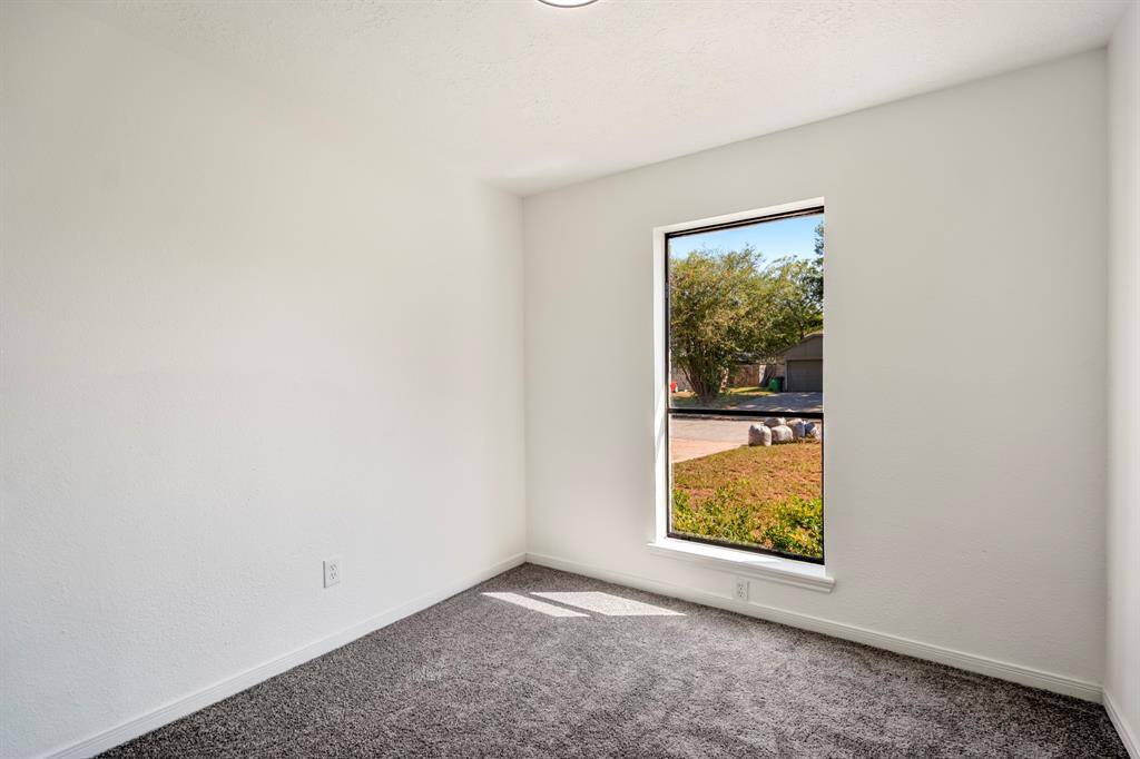 This alternate view of the first bedroom highlights the large window that fills the space with natural light, enhancing the room's bright and airy feel. The combination of the new carpeting and natural light creates a warm and welcoming ambiance.