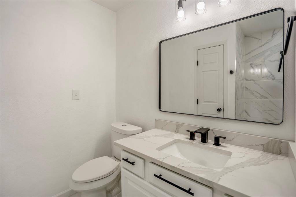 This bathroom exudes modern elegance with its sleek, rounded corner rectangle mirror, adding a contemporary flair to the space. The quartz countertops offer a luxurious touch, complemented by matte black hardware for a bold contrast. A stylish modern light fixture illuminates the room, enhancing its bright and inviting ambiance.