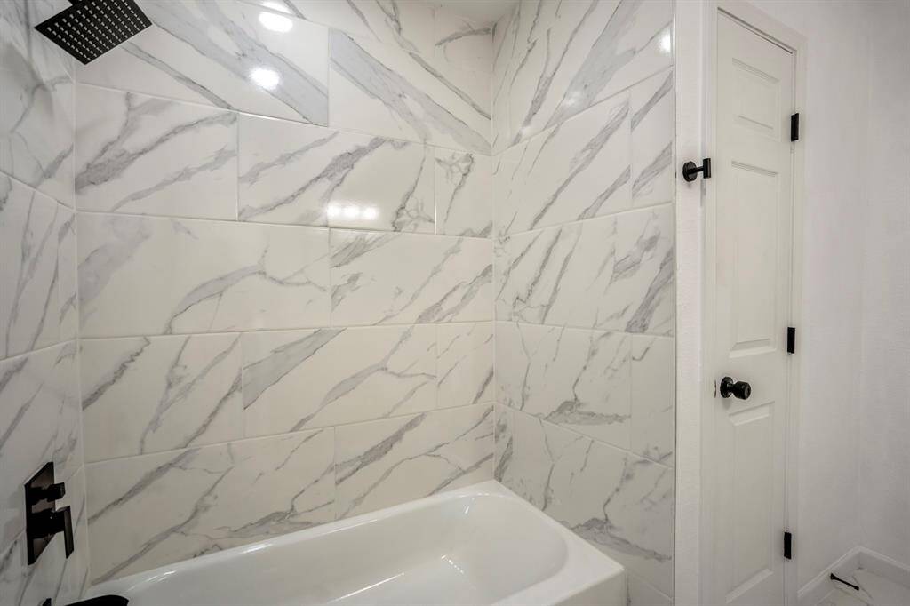 This alternate view of the bathroom reveals the stunning marble-look tile adorning the shower walls, elevating the space with a sense of luxury. The sleek, modern shower head and brand new tub further enhance the high-end appeal, creating a spa-like experience that exudes sophistication and contemporary elegance.