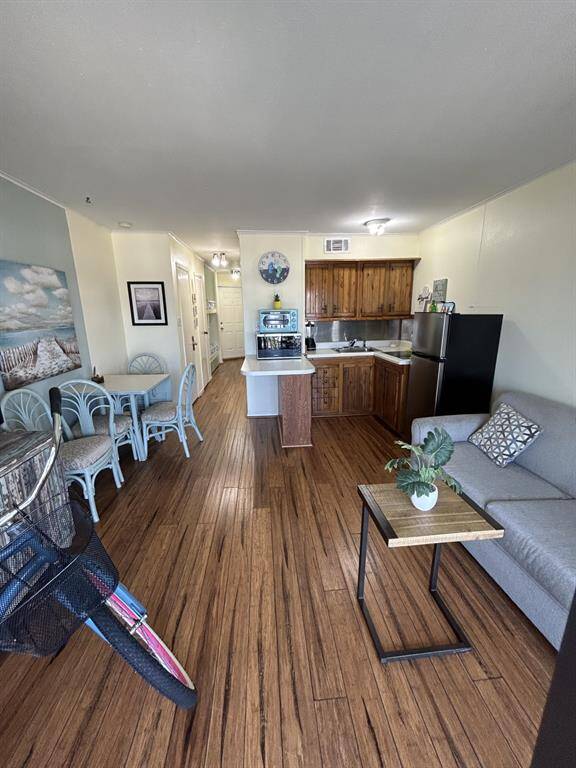 Looking from the balcony through the condo with the condo front door in far background.  Sleeper sofa in the foreground & kitchen area on the right. Look at these beautiful wood plank floors.