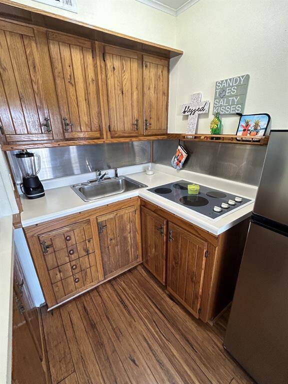 Compact and efficient kitchen with electric cooktop. Refrigerator to the right. Stainless steel backsplash.