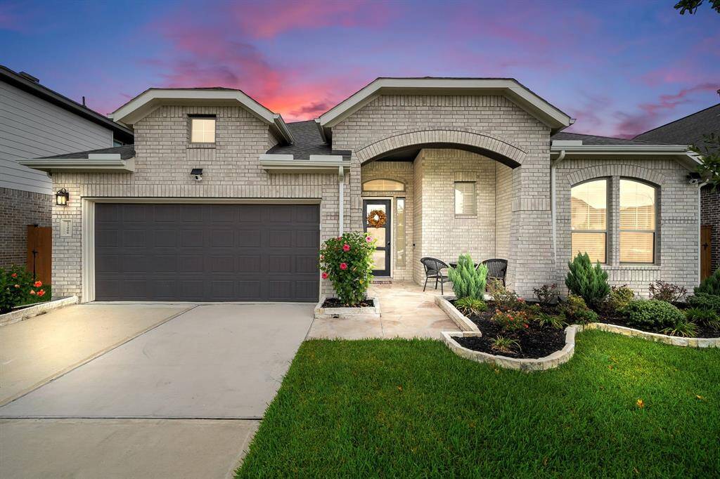 This is a single-story brick home featuring an arched entryway, two-car garage, and neatly landscaped front yard.