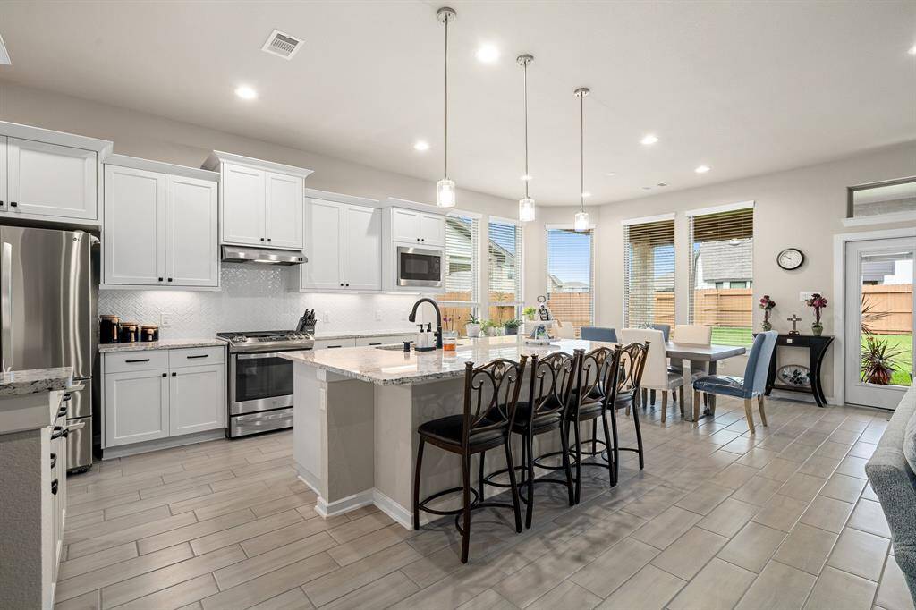 Modern kitchen with white cabinetry, stainless steel appliances, and an island with seating. Adjacent open-plan dining area features ample natural light.