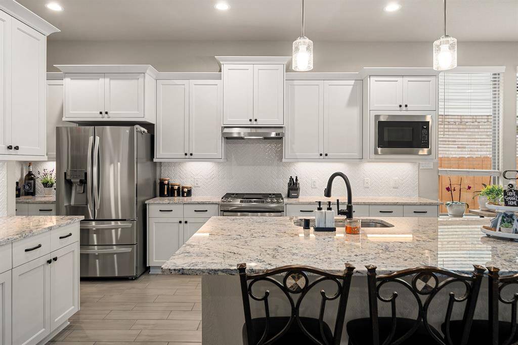 Modern kitchen with stainless steel appliances, white cabinetry, granite countertops, and pendant lighting over a central island with seating area.