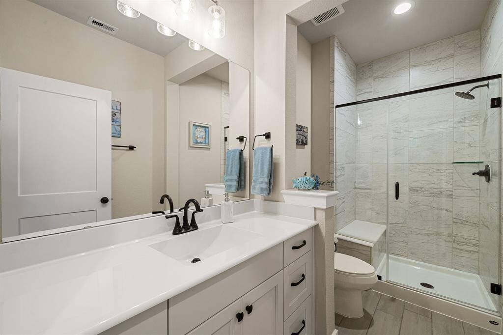 Modern bathroom featuring a vanity with white countertops and cabinetry, sleek black faucets, a large mirror, and a walk-in shower with glass doors and marble-look tiles.