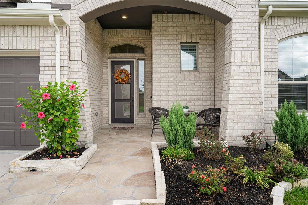 This is a welcoming entryway to a home featuring a custom stamped concrete pathway and porch, complemented by a tastefully landscaped garden with flowering plants and shrubs.
