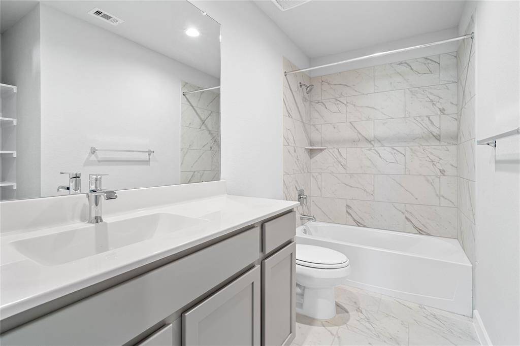 Secondary bath features tile flooring, bath/shower combo with tile surround, stained wood cabinets, beautiful light countertops, mirror, sleek fixtures and modern finishes!