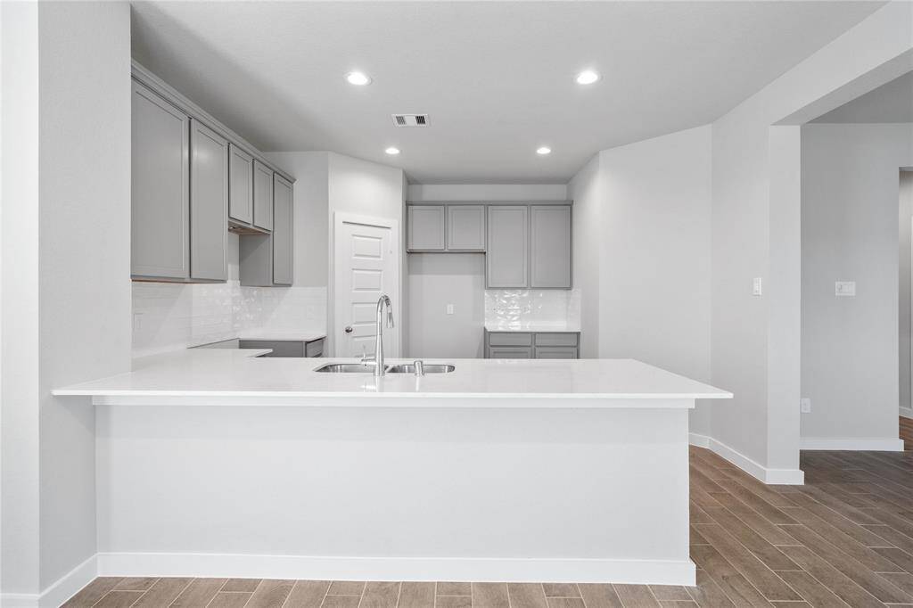 This stunning kitchen features stained cabinets, custom neutral paint, quartz countertops, modern backsplash, breakfast bar, recessed lighting, high ceilings, and walk in pantry!