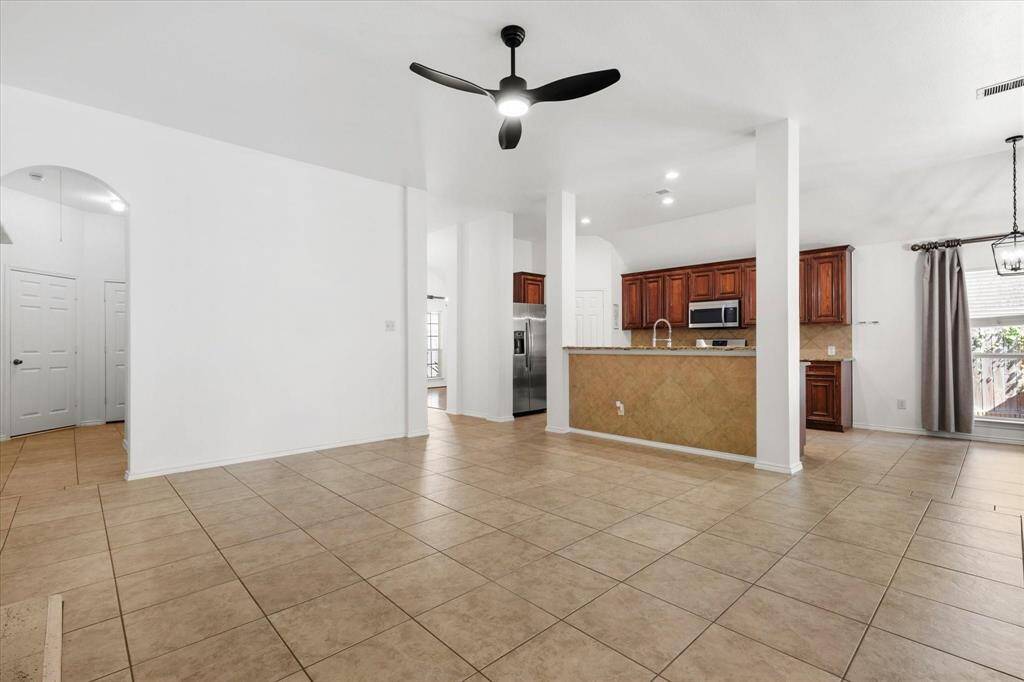 Another view of the kitchen, breakfast and bedroom hallway from the family room. This is a spacious, open-plan living area with tile flooring, a modern kitchen with wooden cabinetry and a breakfast bar.