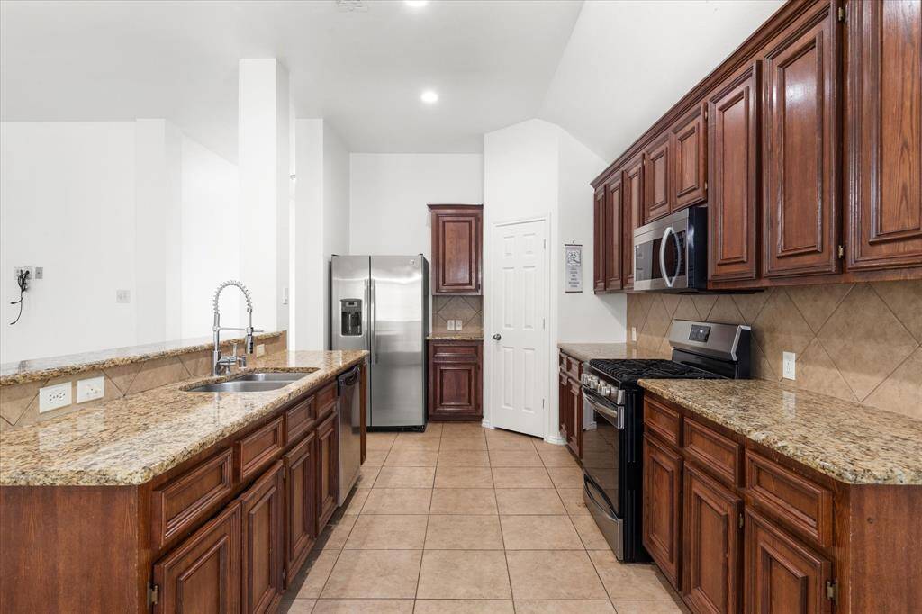 The kitchen has a spacious pantry. This is a modern kitchen featuring granite countertops, stainless steel appliances, and rich-toned wooden cabinets. There's a gas range, built-in microwave. The kitchen also includes a deep sink with a high arc faucet and a tile backsplash, here's plenty of storage space.