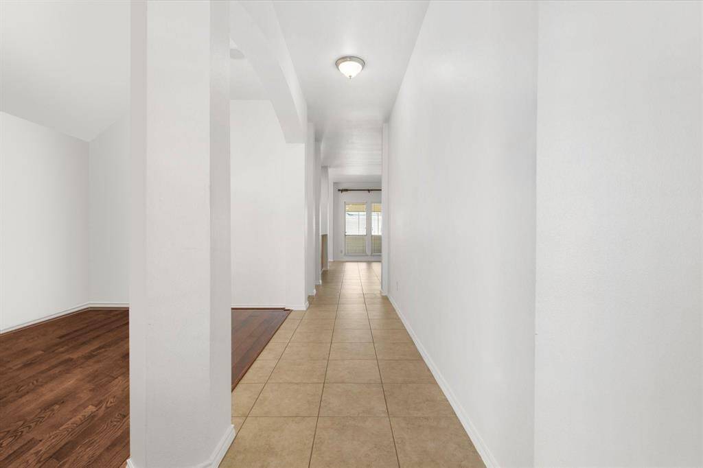 These walls would be perfect to show off your artwork or family photos. This is a well-lit, spacious hallway featuring clean white walls, a combination of tile and hardwood flooring. It leads to the family room , suggesting a warm, inviting atmosphere.