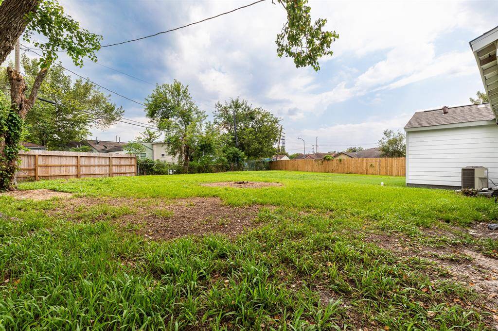 This is a spacious backyard with a mix of green lawn and some bare patches, bordered by a wooden fence and featuring a mature tree, offering potential for landscaping or outdoor living space adjacent to a white-sided house.