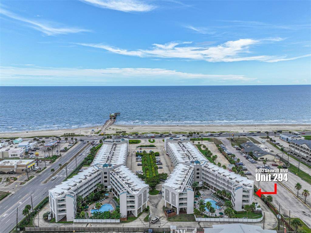 Aerial view of Casa Del Mar promising convenient beach access and amenities such as a pool, indicated by the visible outdoor spaces. The area includes nearby parking and easy access to a main thoroughfare. The property has an unobstructed view of the beach from the balcony.