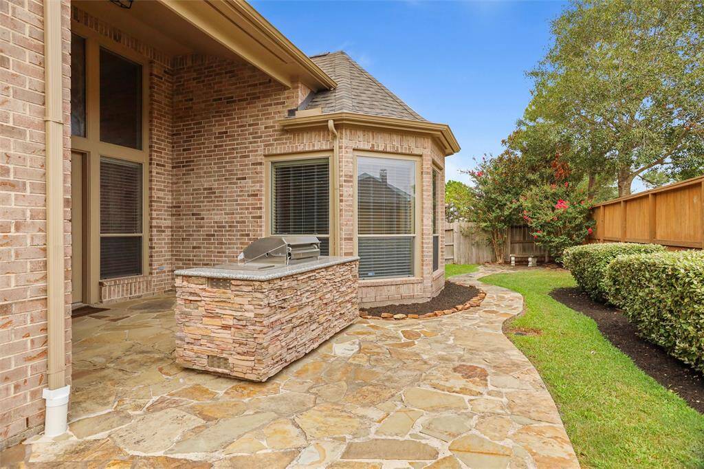 This is a well-maintained backyard with a stone patio, built-in grill, and lush landscaping, offering a private outdoor space for relaxation and entertainment.