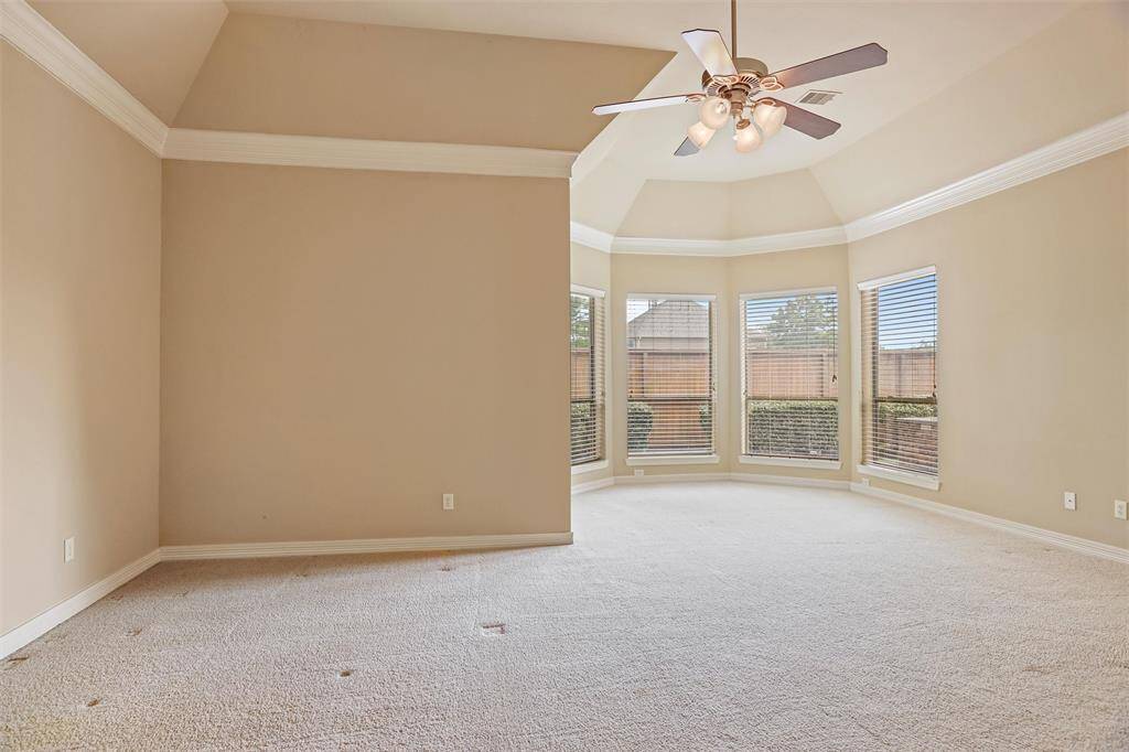 This is a spacious room with high ceilings, carpet flooring, and a ceiling fan. It features a bay window providing plenty of natural light.