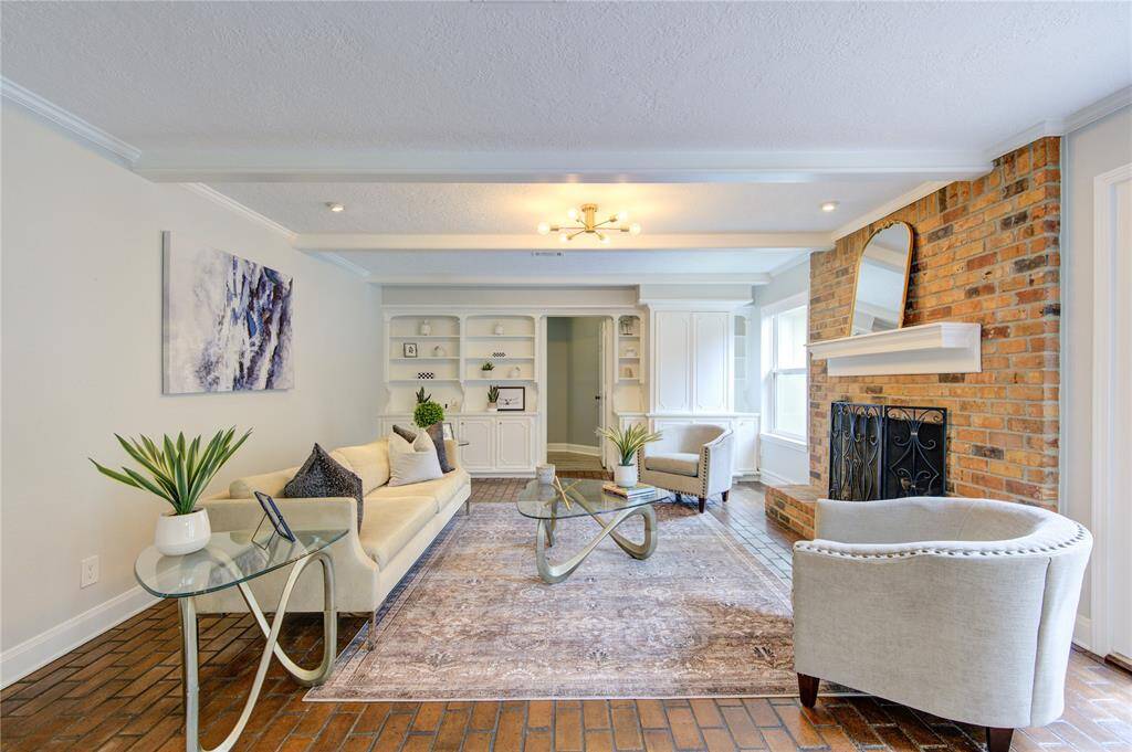 This inviting living room features a cozy brick fireplace, built-in shelving, and ample natural light. The space is elegantly furnished with a neutral-toned sofa, armchairs, and modern glass tables, creating a warm and stylish atmosphere.