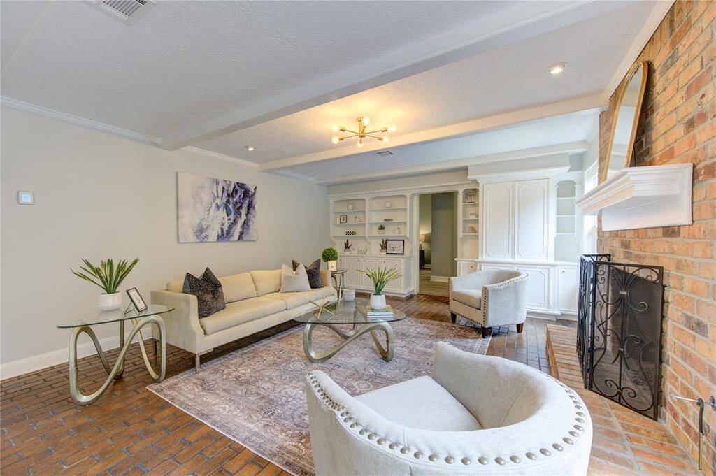 This cozy living room features a brick fireplace, elegant built-in shelving, and a blend of modern and classic decor. The space is bright and inviting, with comfortable seating and stylish accents.