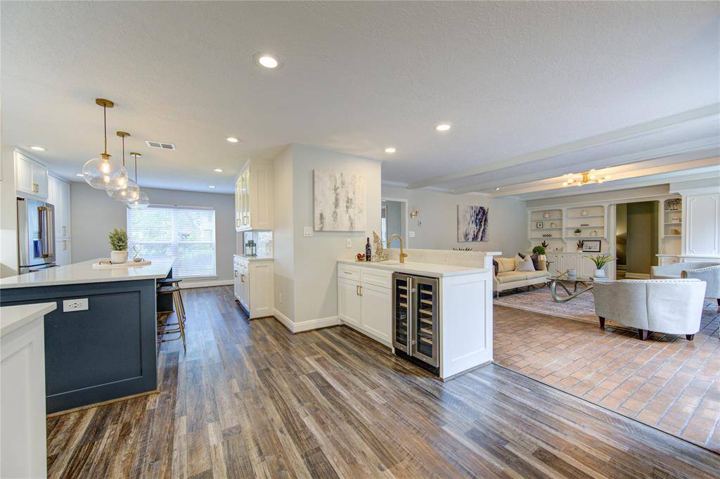 This photo showcases a spacious, open-concept kitchen and living area. It features modern lighting, hardwood floors, and a sleek island with bar seating. The living room includes built-in shelving and a cozy seating area, creating a welcoming, functional space.