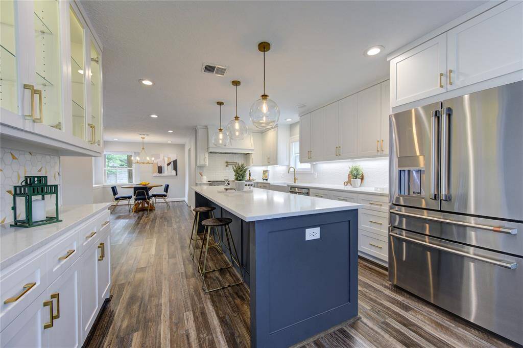 This modern kitchen features sleek stainless steel appliances, a large island with seating, and elegant pendant lighting. The open layout flows into a dining area, and the space is accented with light cabinetry and hardwood floors. Perfect for entertaining.