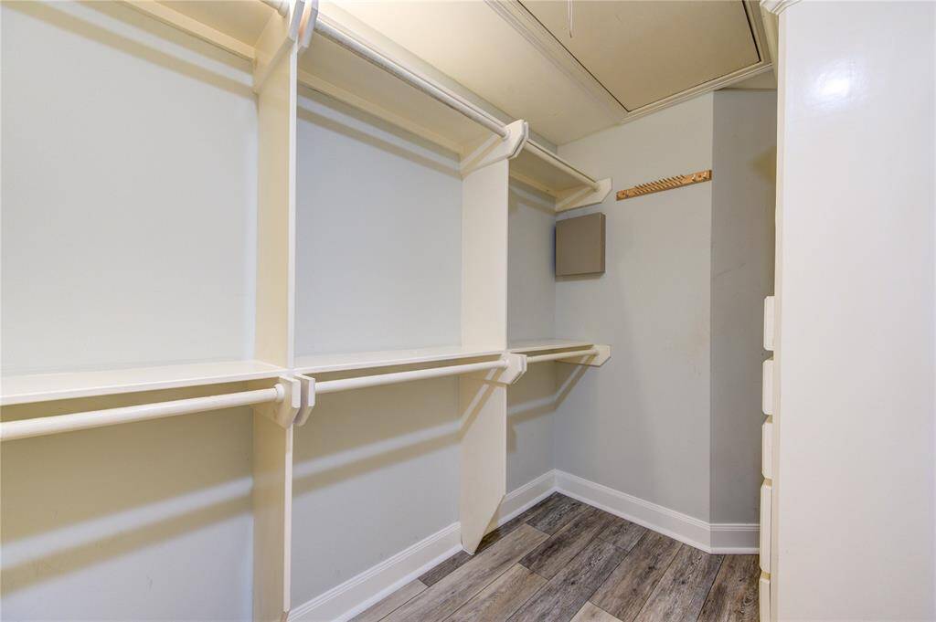 This photo shows a spacious walk-in closet with multiple shelves and hanging rods, featuring light-colored walls and wood-look flooring.