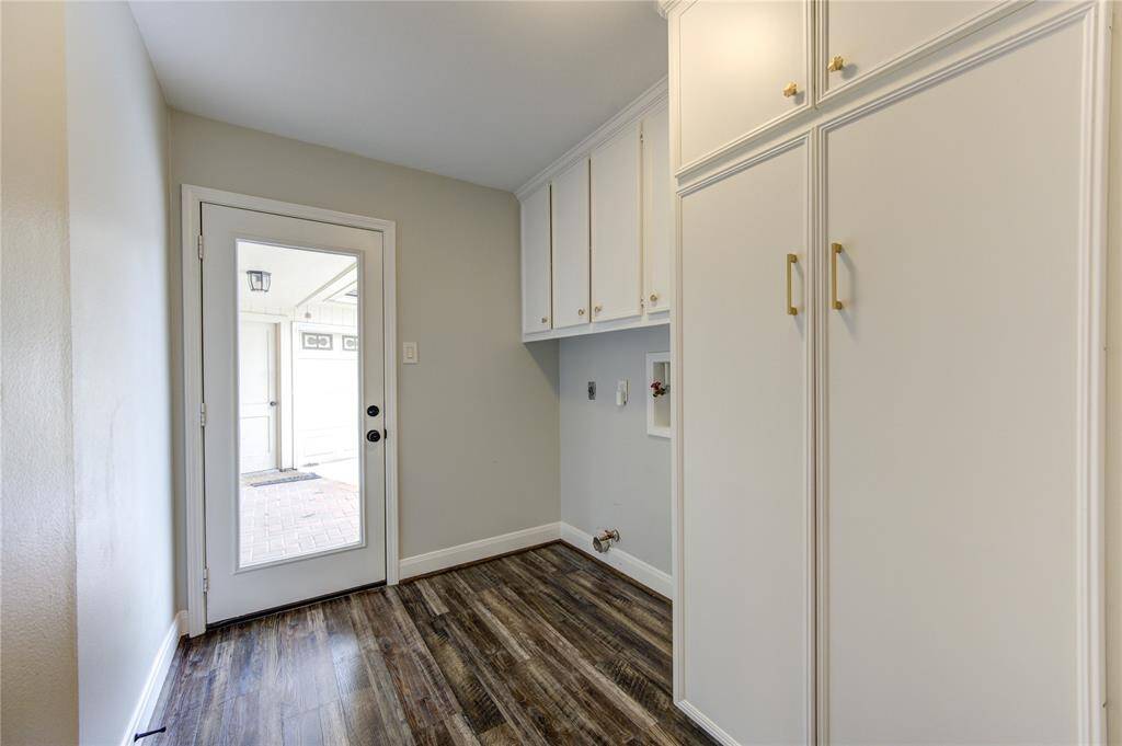 This photo shows a bright utility room with white cabinetry for ample storage, a door leading outside, and wood-look flooring. Perfect for laundry and storage needs.