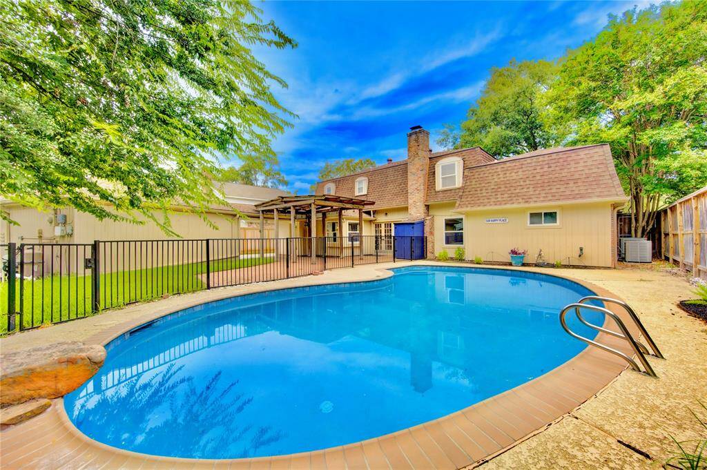 This charming backyard features a spacious pool, surrounded by lush greenery and a cozy patio area, perfect for outdoor relaxation and entertaining. The home exterior has a rustic feel with a chimney and a fenced yard for added privacy.