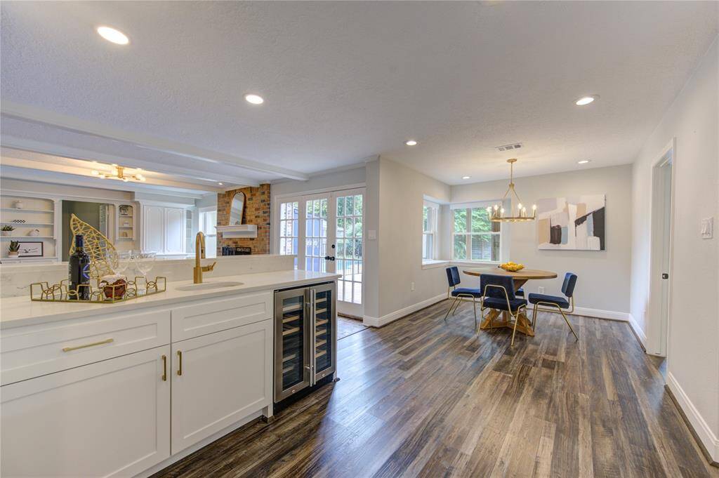 This inviting open-concept kitchen and dining area features modern white cabinetry, a built-in wine cooler, and stylish wood flooring. Natural light fills the space through large windows and glass doors, enhancing the cozy dining nook.