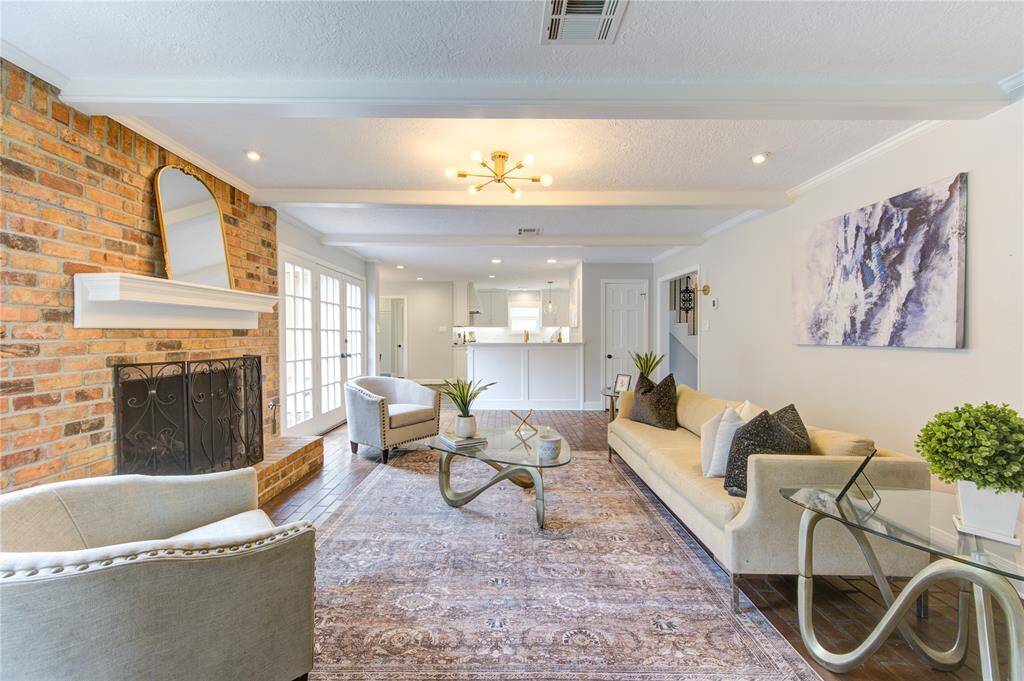 This inviting living room features a cozy brick fireplace, elegant recessed lighting, and stylish decor. Large windows provide ample natural light, and the open layout flows seamlessly into a modern kitchen, perfect for entertaining.